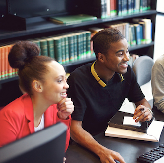 Diverse group of students using computer for finding information for their academic project. Happy young people sitting at table with books and computer taking notes for their study.