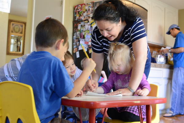 family child care provider bends over preschool girl looking at artwork