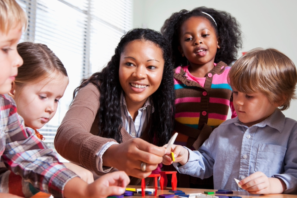 Teacher smiling with students at table playing with toys.