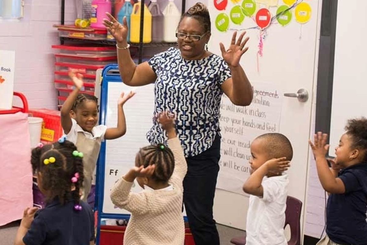 Teacher and students standing in circle with both hands raised and smiling